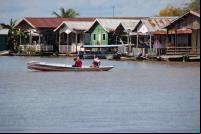homem e mulher navegam de barco em frente a casas na beira de rio
